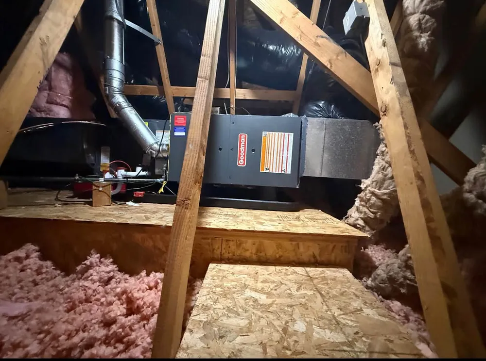 Furnace in an attic between wooden joists with pink insulation
