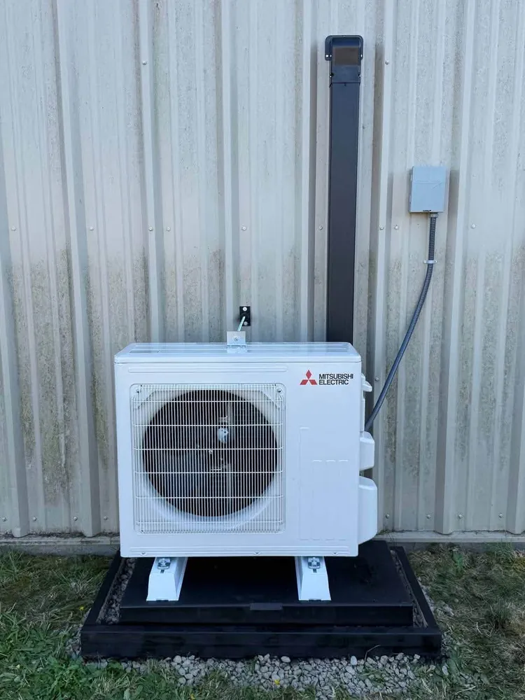 White ductless outdoor unit on a black pad against pale siding