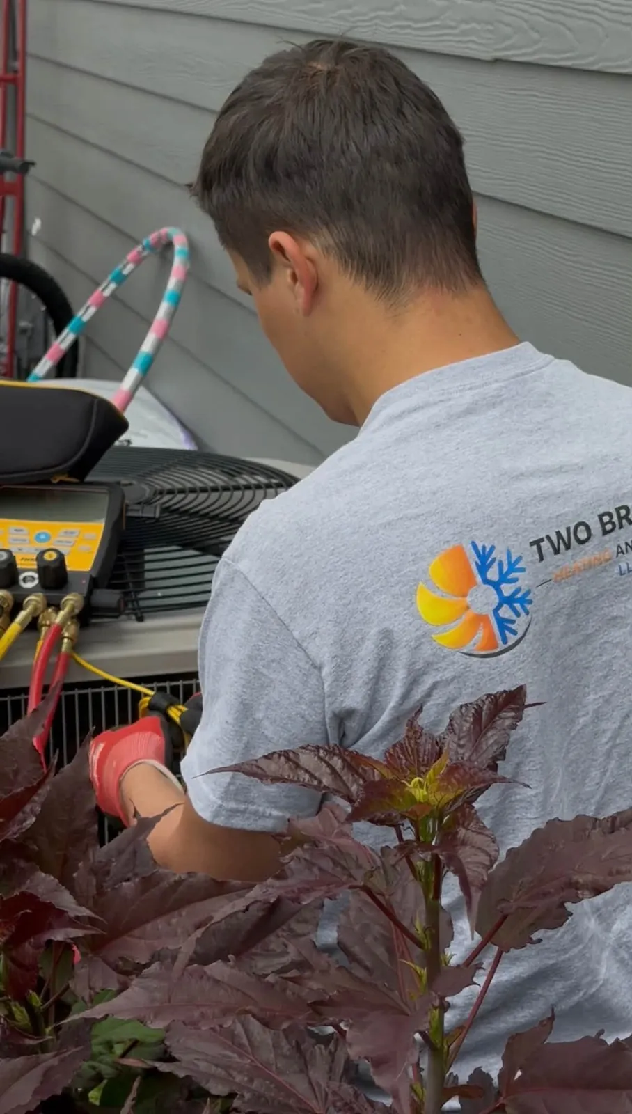 Technician in a gray work shirt servicing equipment beside garden plants
