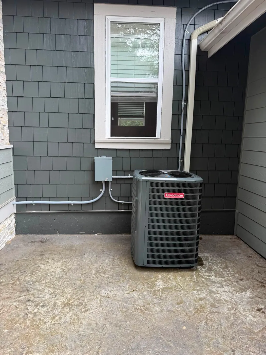 Outdoor condenser beside gray-blue siding with an electrical disconnect box